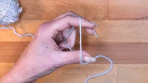 Lege den Faden vom Knäuel kommend über Zeigefinger und Daumen der linken Hand und halte beide Enden mit Ringfinger und kleinem Finger fest.. Maschen Anschlagen