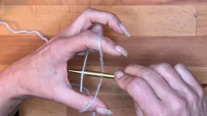 Führe die Nadel in die Lücke zwischen Faden und Hand und hole den unteren Daumenfaden nach oben.. Maschen Anschlagen