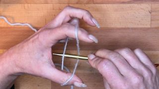 Führe die Nadel in die Lücke zwischen Faden und Hand und hole den unteren Daumenfaden nach oben. maschen anschlagen