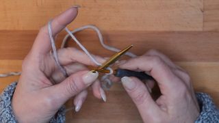 Lege deine Stricknadel auf den Arbeitsfaden hinter die Häkelnadel.  maschen anschlagen