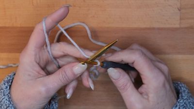 Lege deine Stricknadel auf den Arbeitsfaden hinter die Häkelnadel.  maschen anschlagen