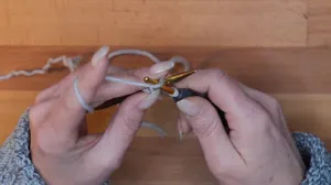 Hole den Faden über die Nadel mit der Häkelnadel und ziehe ihn durch die Schlaufe auf der Häkelnadel. Der Arbeitsfaden befindet sich jetzt vor der Stricknadel.. Maschen Anschlagen