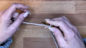 Starte mit einem Laufknoten auf der Nadel in der rechten Hand und halte den Arbeitsfaden mit Ringfinger und kleinem Finger der rechten Hand fest.. Maschen Anschlagen