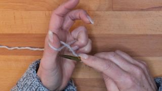 Lege den Arbeitsfaden von unten nach oben um den Daumen, sodass eine Schlaufe um den Daumen entsteht. maschen anschlagen