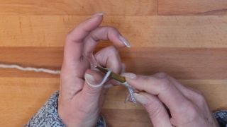 Steche mit der Nadel von unten nach oben in diese Daumenschlinge und lass sie auf die Nadel gleiten. maschen anschlagen