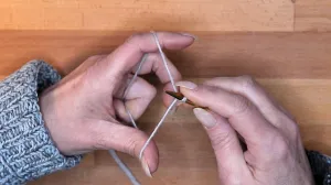 Starte mit einem Laufknoten mit langem Anfangsfaden und lege den Laufknoten über die Nadel in deiner rechten Hand, sodass der Anfangsfaden zu dir hin zeigt und der Arbeitsfaden von dir weg.. Maschen Anschlagen