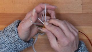 Führe die Nadel unterhalb vom Daumen von unten nach oben durch die Daumenschlinge. maschen anschlagen