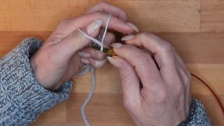 Hole den Faden vom Zeigefinger mit der Nadel durch die Daumenschlaufe. maschen anschlagen