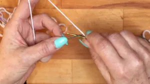 Hole mit der Nadel den Arbeitsfaden unter dem Hilfsfaden durch. . Maschen Anschlagen