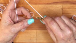 Hole mit der Nadel den Arbeitsfaden unter dem Hilfsfaden durch.  maschen anschlagen