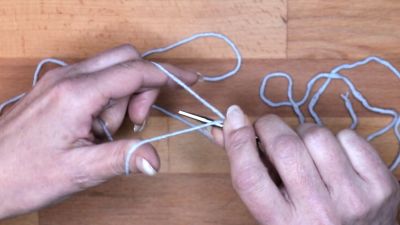 Führe die Nadel unter den Daumenfaden und hole den Faden vom Zeigefinger. Achte darauf, dass der Daumenfaden gespannt bleibt. Das ist die zweite Masche.  maschen anschlagen